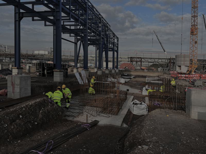 Bauarbeiter bei Fundamentarbeiten auf einer Industriebaustelle mit Stahlkonstruktion